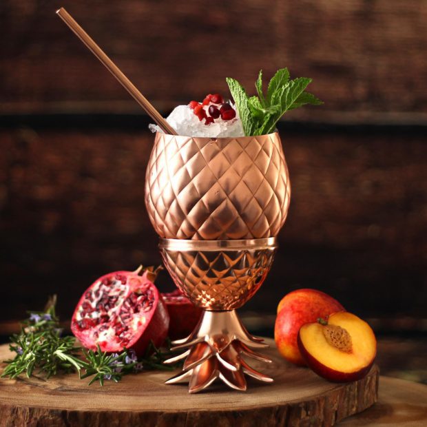 copper pineapple vessel with cocktail and copper drinking straw
