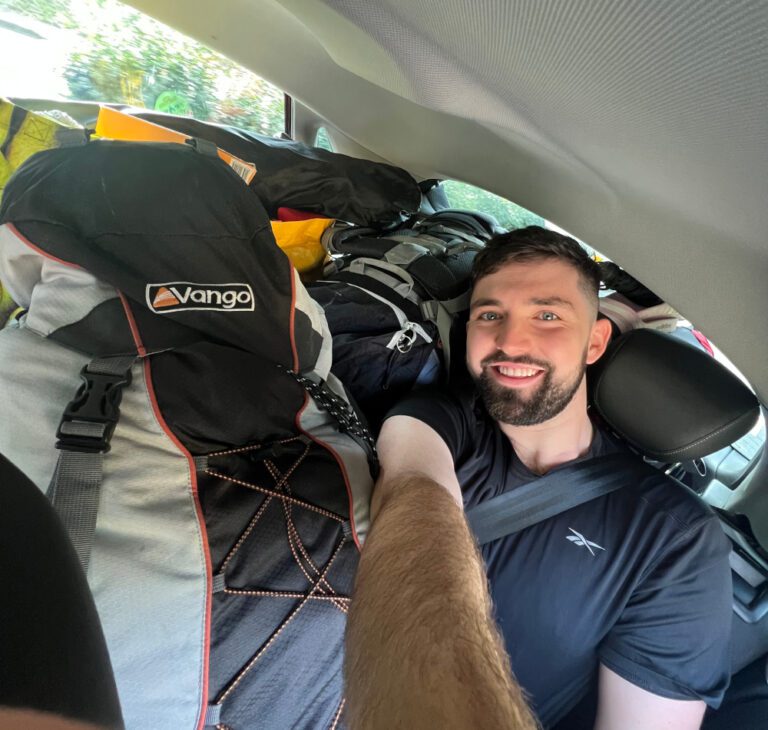 Young man in a car surrounded by camping pack and tent for working at a festival