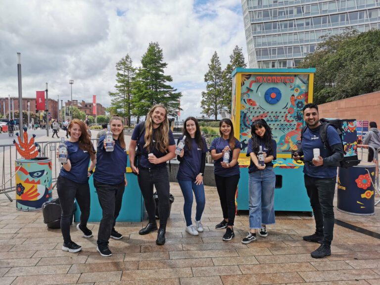 HEL' Event staff all dressed in dark blue and posing with bottles of Tequila. In front of a brightly coloured bar