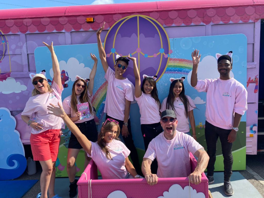 work colleagues dressed in pink teeshirts in front of giant kids dollhouse part of an immersive roadshow experience