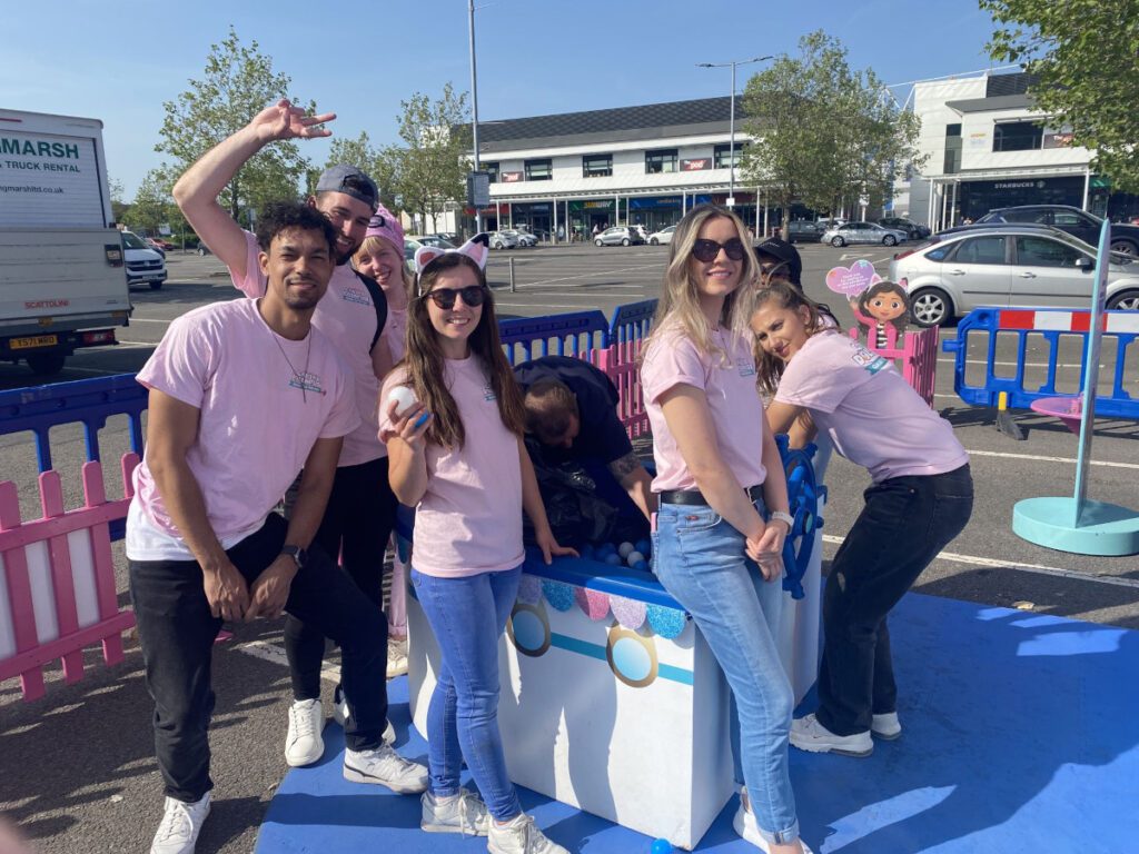 People dressed in pink teeshirts in front of giant kids dollhouse part of an immersive roadshow experience